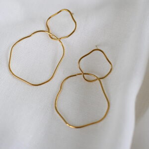 Goudkleurige oorhangers met dubbele open vormen op wit textiel