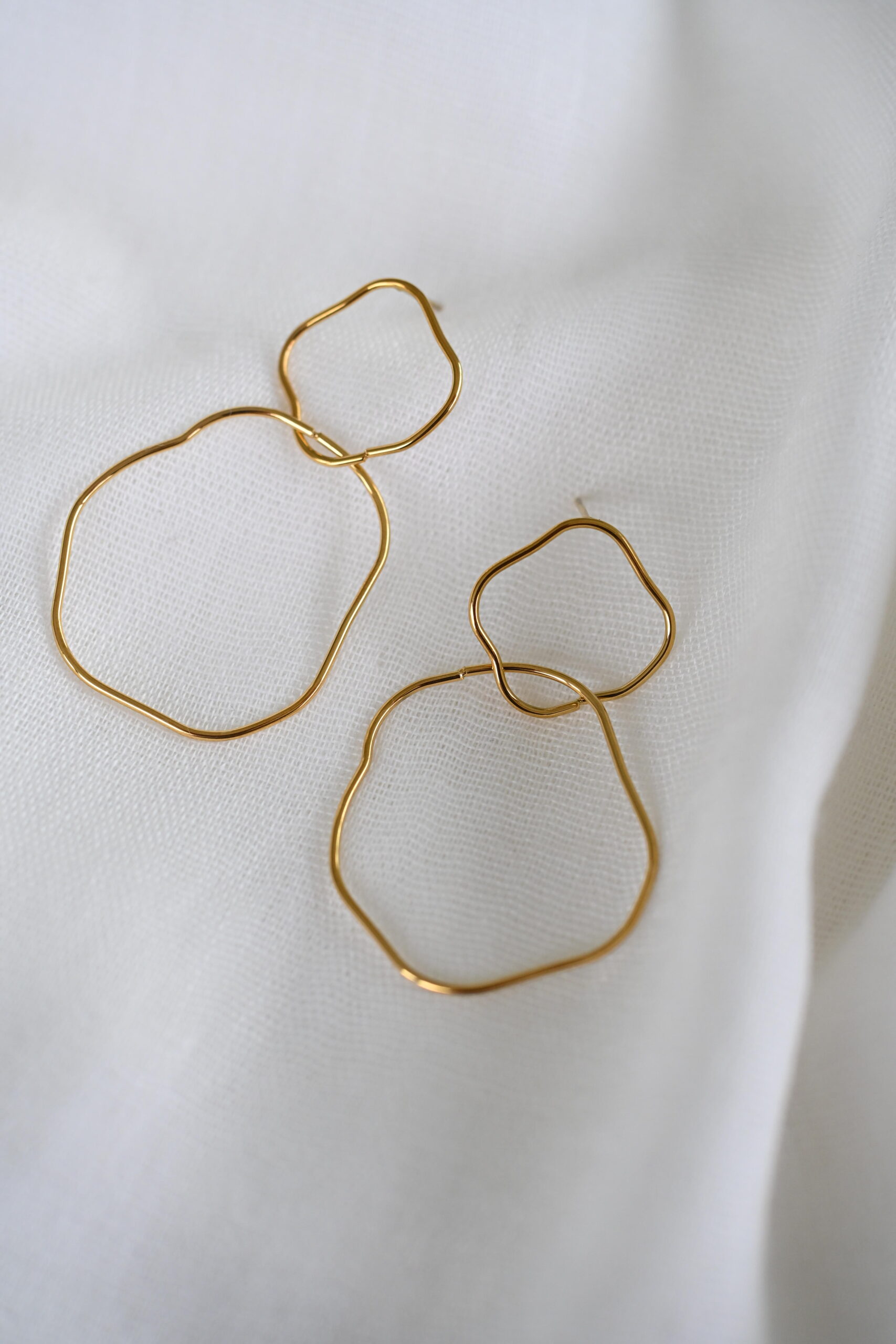 Goudkleurige oorhangers met dubbele open vormen op wit textiel