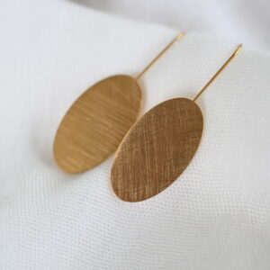 Goudkleurige ovale oorhangers op wit textiel