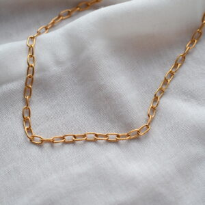Goudkleurige stainless steel ketting met fijne langwerpige ovale schakels op lichte stof